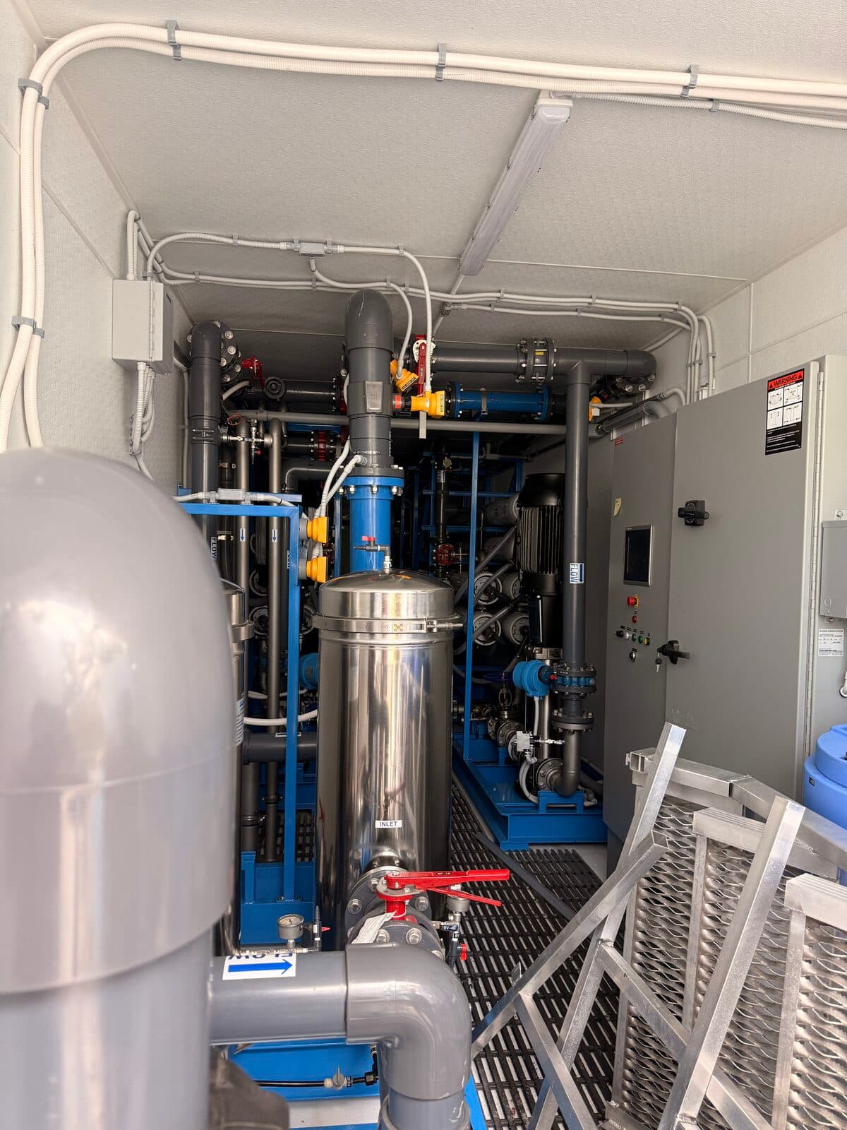 Inside containerized RO water treatment system at Falcon Water Tech — stainless steel vessels, blue pumps, piping